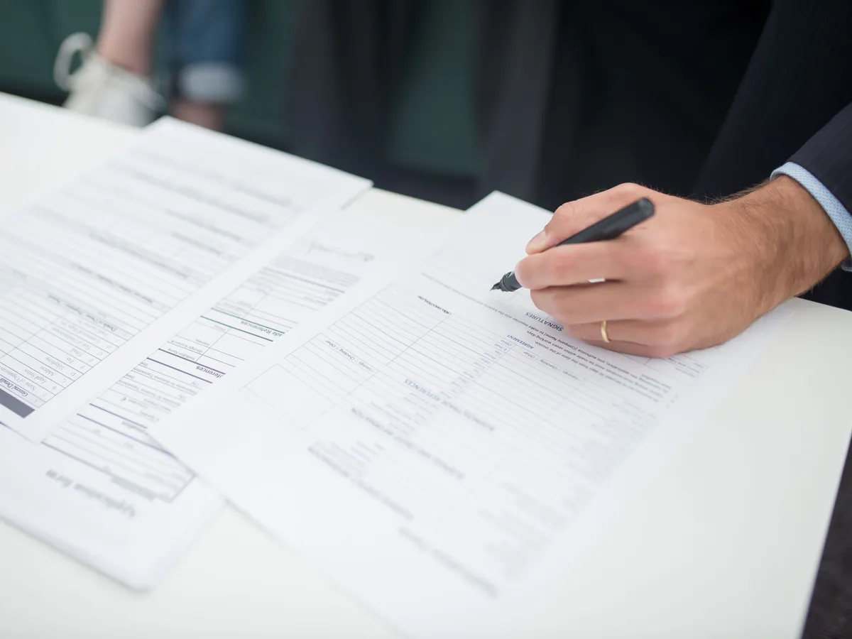 Main signant un document administratif au stylo sur un bureau