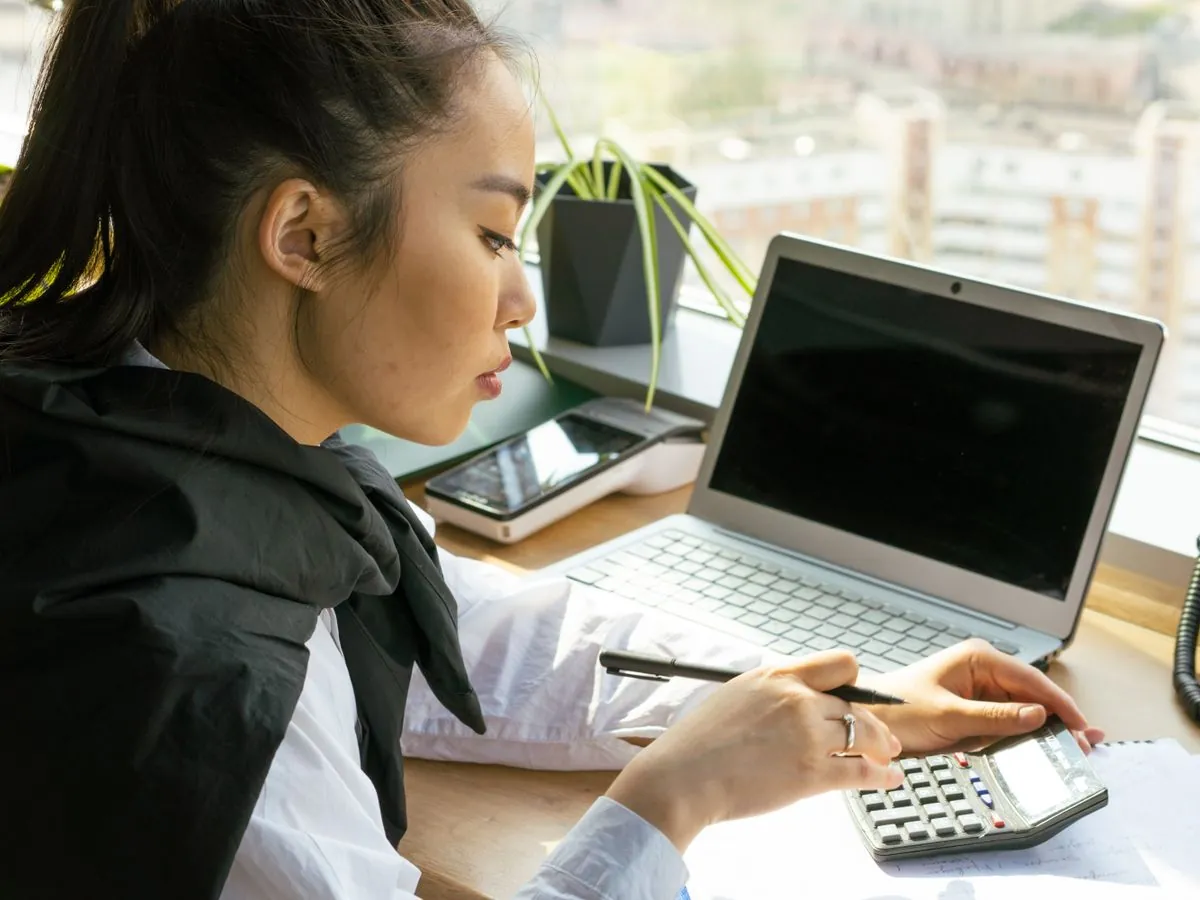 Professionnelle saisissant des données chiffrées sur une calculatrice à son bureau, à côté d'un ordinateur portable