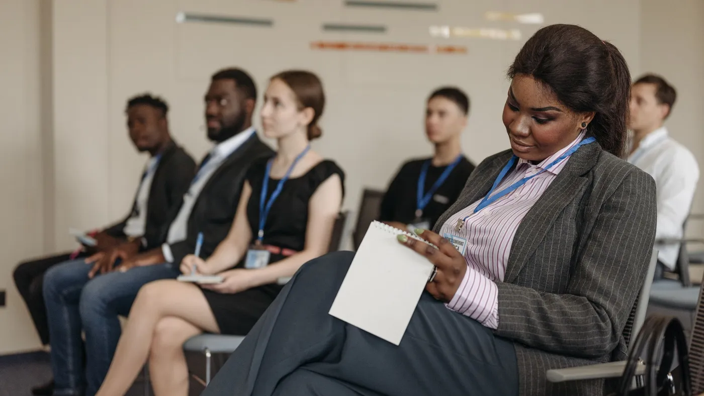 Participants d'une session de formation professionnelle assis en rang, une stagiaire prend des notes