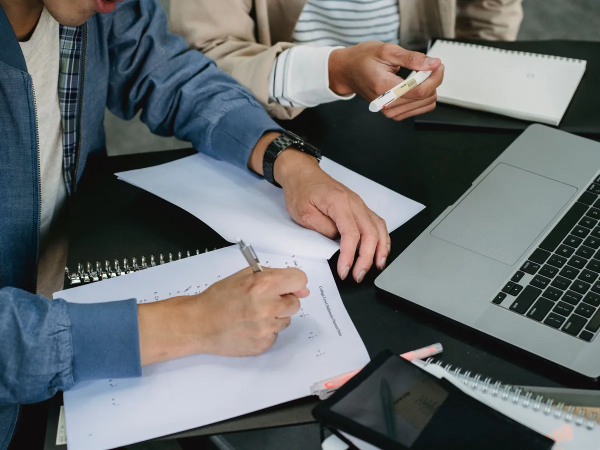Mains annotant un support pédagogique papier à côté d'un ordinateur portable