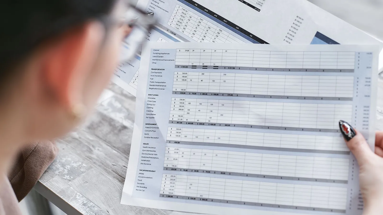 Personne vérifiant un tableau de suivi financier imprimé, tenu à la main