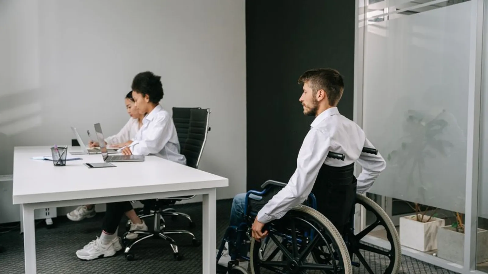 Collaborateur en fauteuil roulant dans une salle de réunion avec deux collègues travaillant sur ordinateur