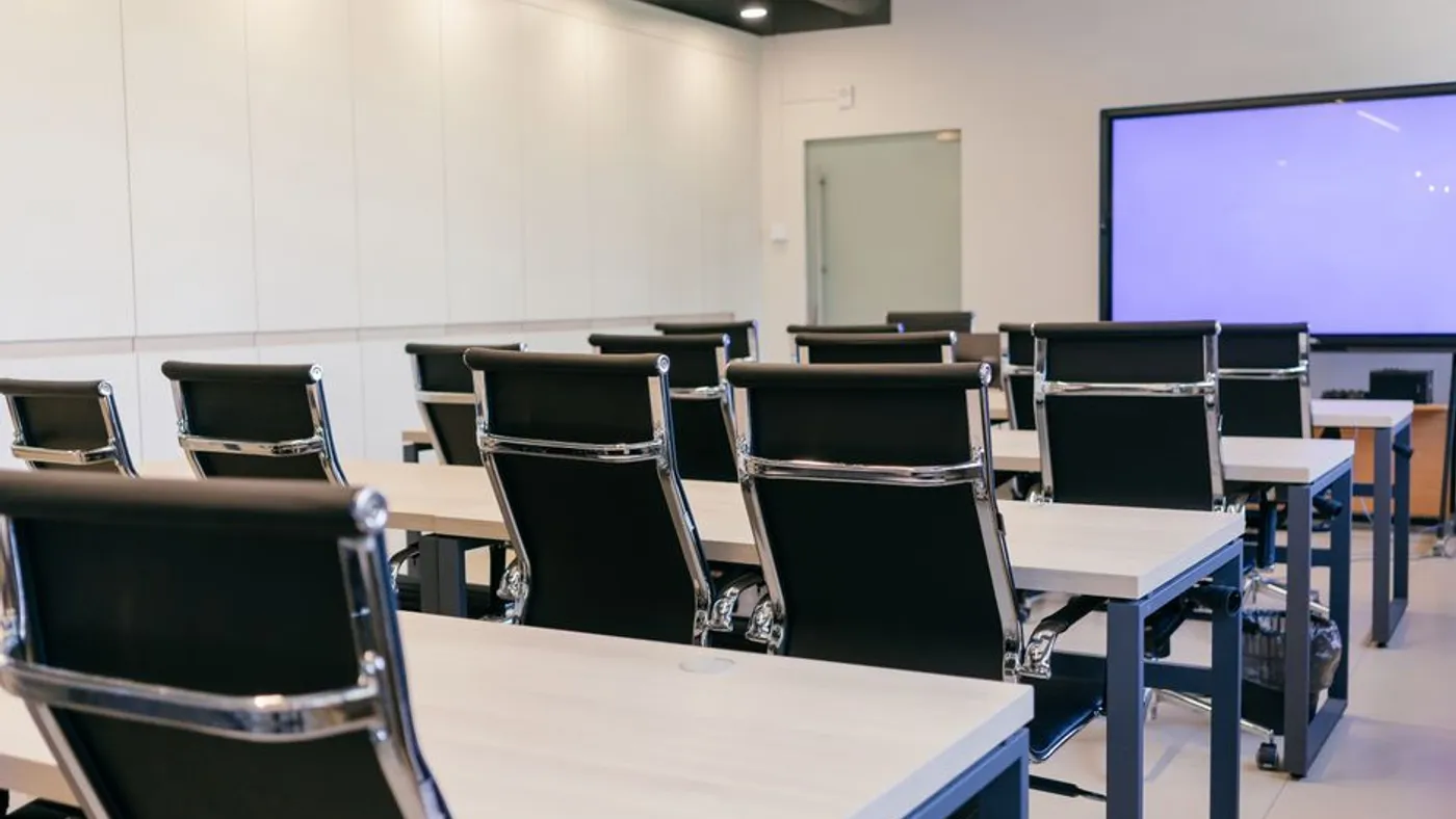 Salle de formation professionnelle vide, équipée de tables et d'un écran